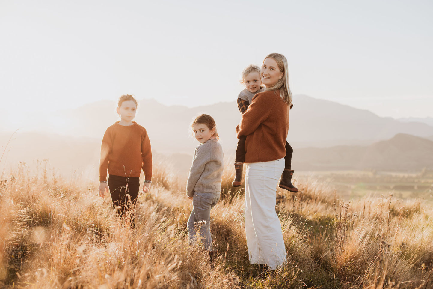 Three children and a lady standing on a hill wearing McIvor Hill lambswool sweaters in rust and grey.