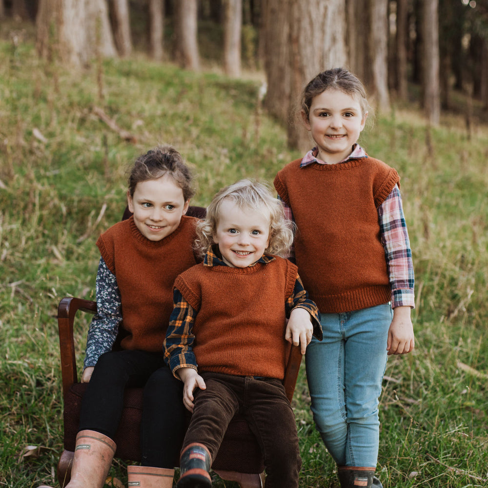 Three children in a forest wearing McIvor Hill lambs' wool knit vests in rust