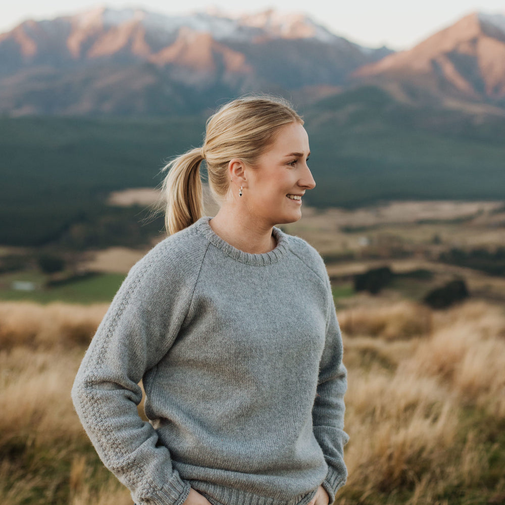 Lady standing up on a hill wearing a McIvor Hill lambs' wool Mabel sweater in grey