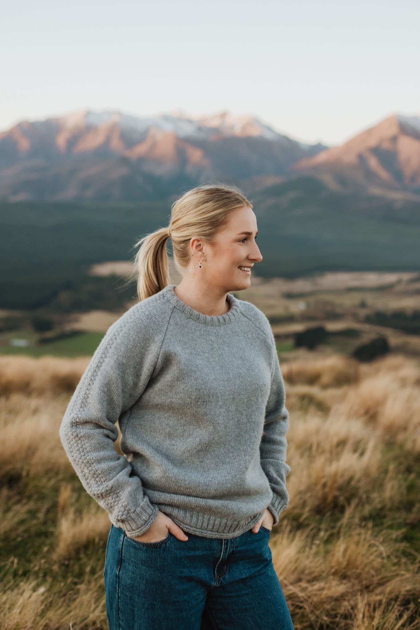 Lady standing up on a hill wearing a McIvor Hill lambs' wool Mabel sweater in grey