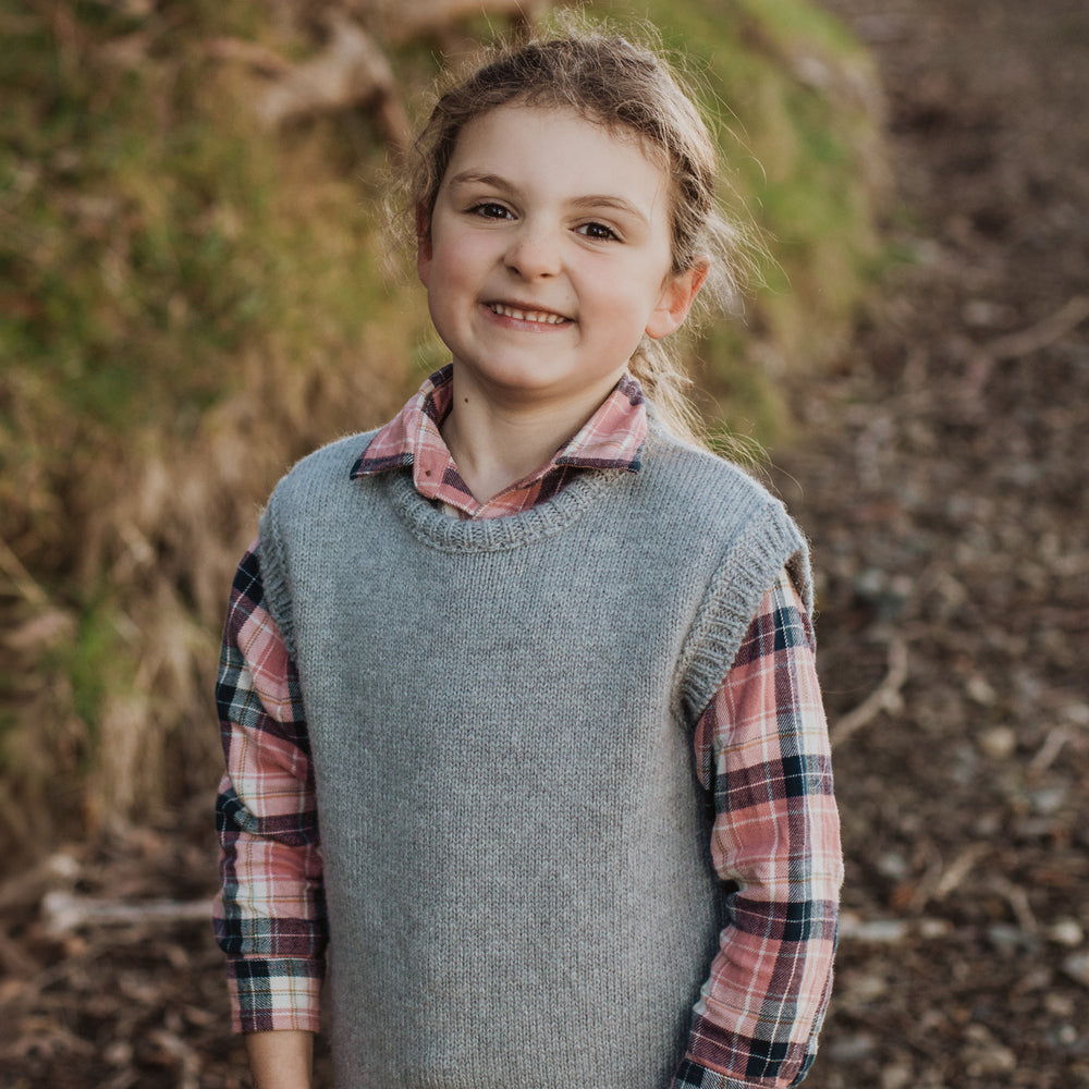 
                      
                        Girl standing in a forest road wearing a McIvor Hill lambs' wool everyday vest in grey.
                      
                    