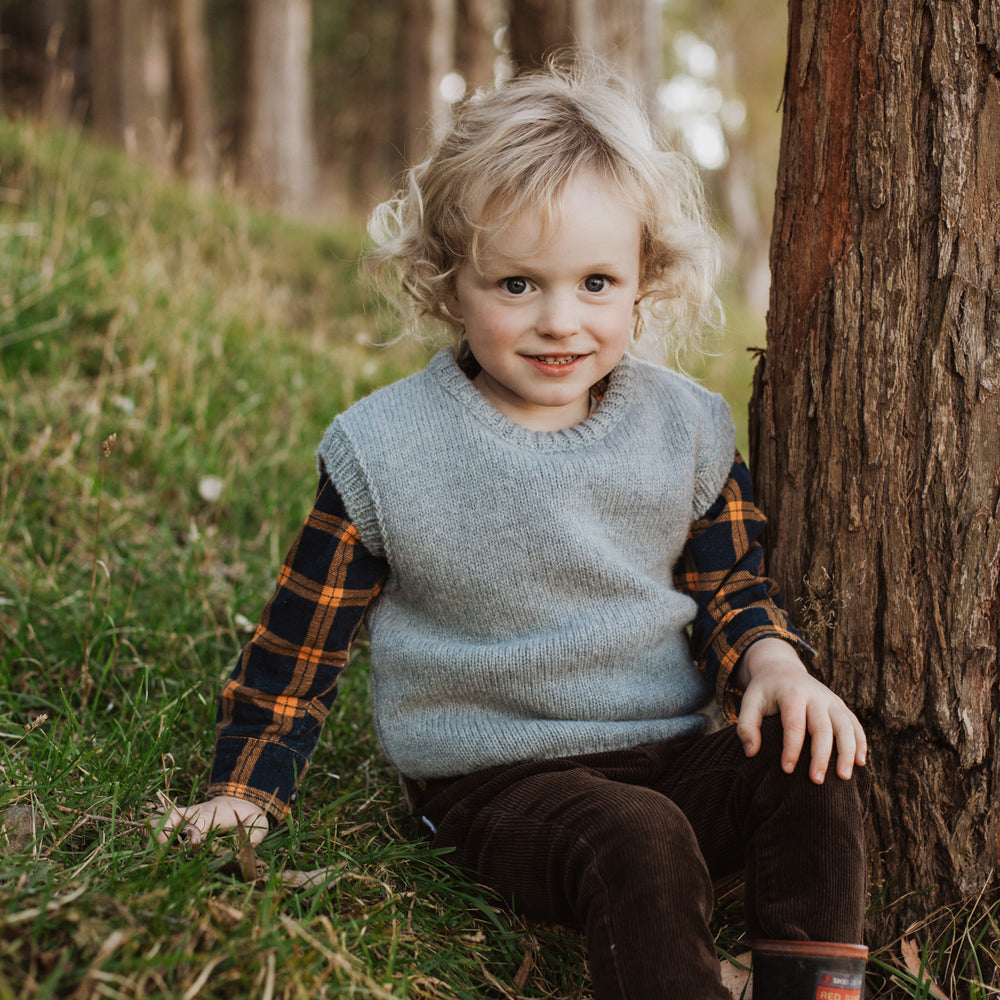 
                      
                        Boy sitting beside a tree wearing a McIvor Hill lambs' wool vest in grey.
                      
                    