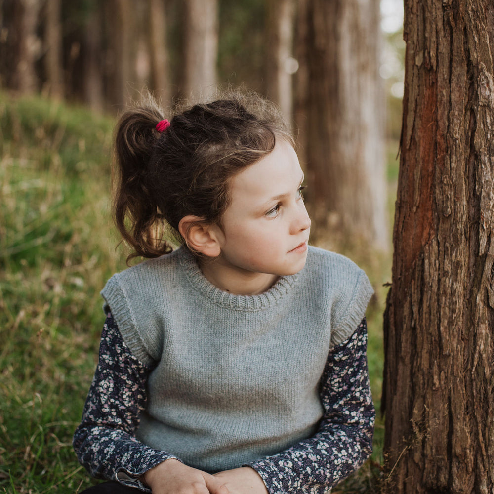 
                      
                        Girl sitting beside a tree wearing a McIvor Hill lambs' wool vest in grey.
                      
                    