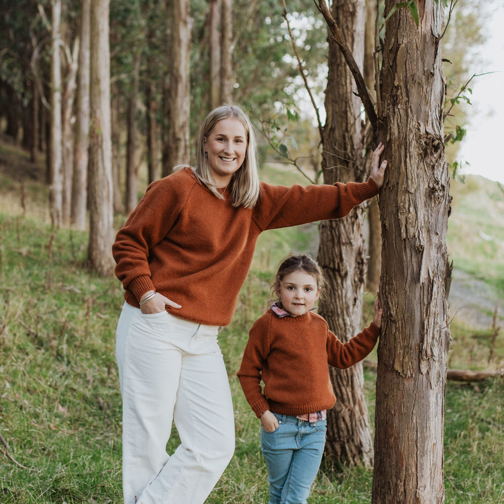 
                      
                        Lady and girl both leaning against a tree wearing McIvor Hill lambs' wool sweaters in rust.
                      
                    