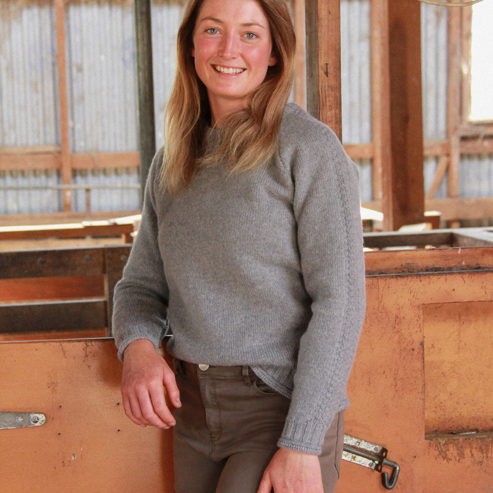 Lady standing in wool shed wear a McIvor Hill Mabel wool sweater in grey.