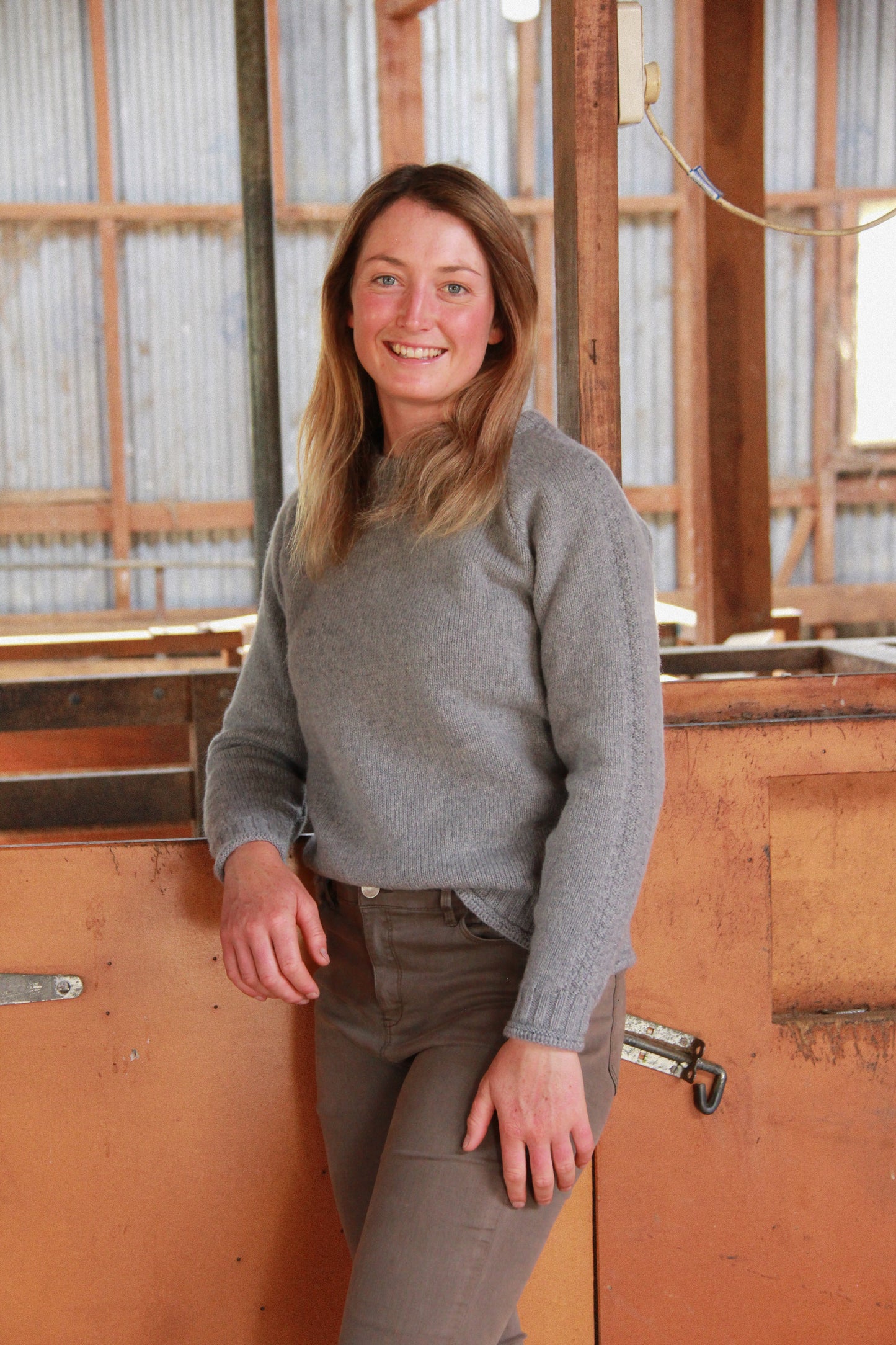 Lady standing in wool shed wear a McIvor Hill Mabel wool sweater in grey.