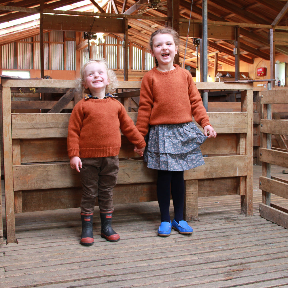 Two kids holding hands laughing in a woolshed