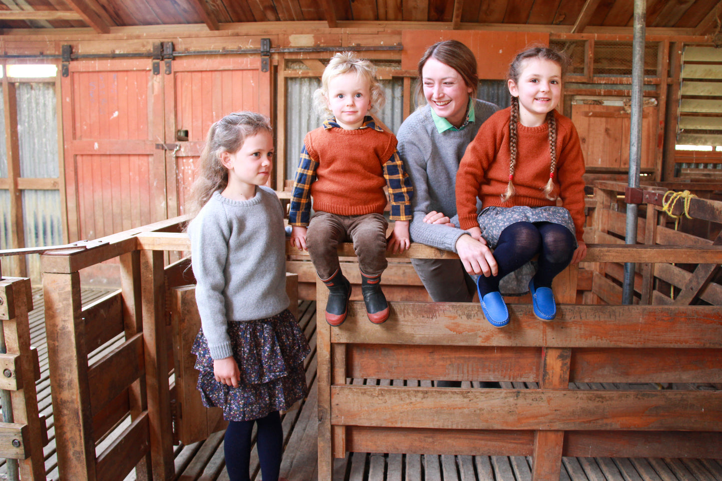 Children with a lady sitting on rails in a woolshed wearing McIvor Hill wool garments