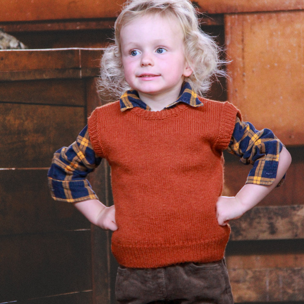 Boy standing in a woolshed with hands on hips wearing a McIvor Hill wool vest in rust