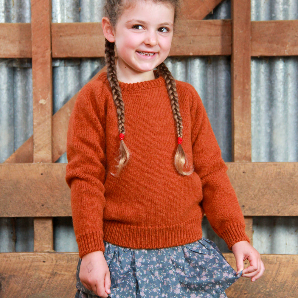 Girl standing in woolshed wearing McIvor Hill wool sweater in rust