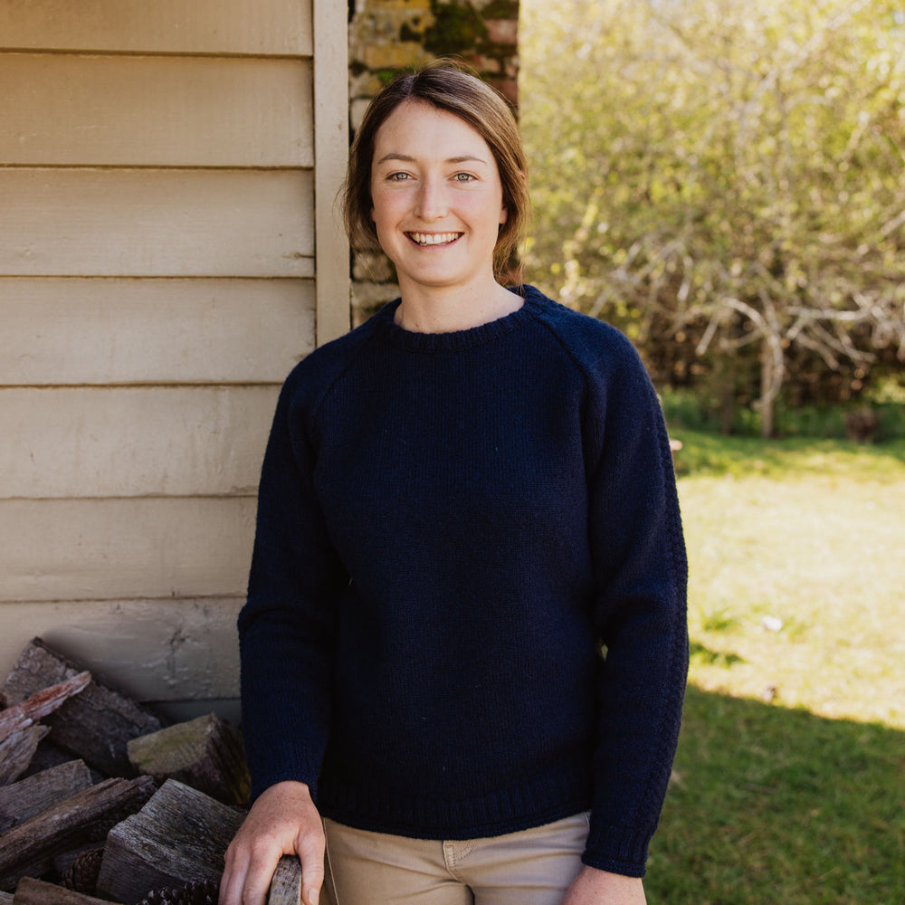 
                  
                    Lady standing by a old shed and fire wood pile wearing a McIvor Hill lambswool Mabel sweater in Navy.
                  
                